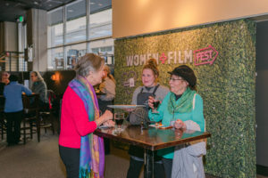 people drinking from cups in front of a Women+Film banner