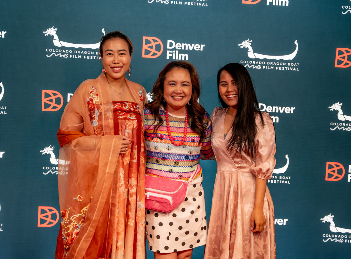 Three women smiling at Colorado Dragon Boat Film Festival backdrop