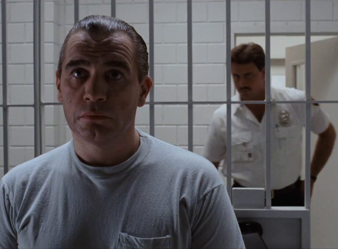 Man in a prison cell with an officer in the background
