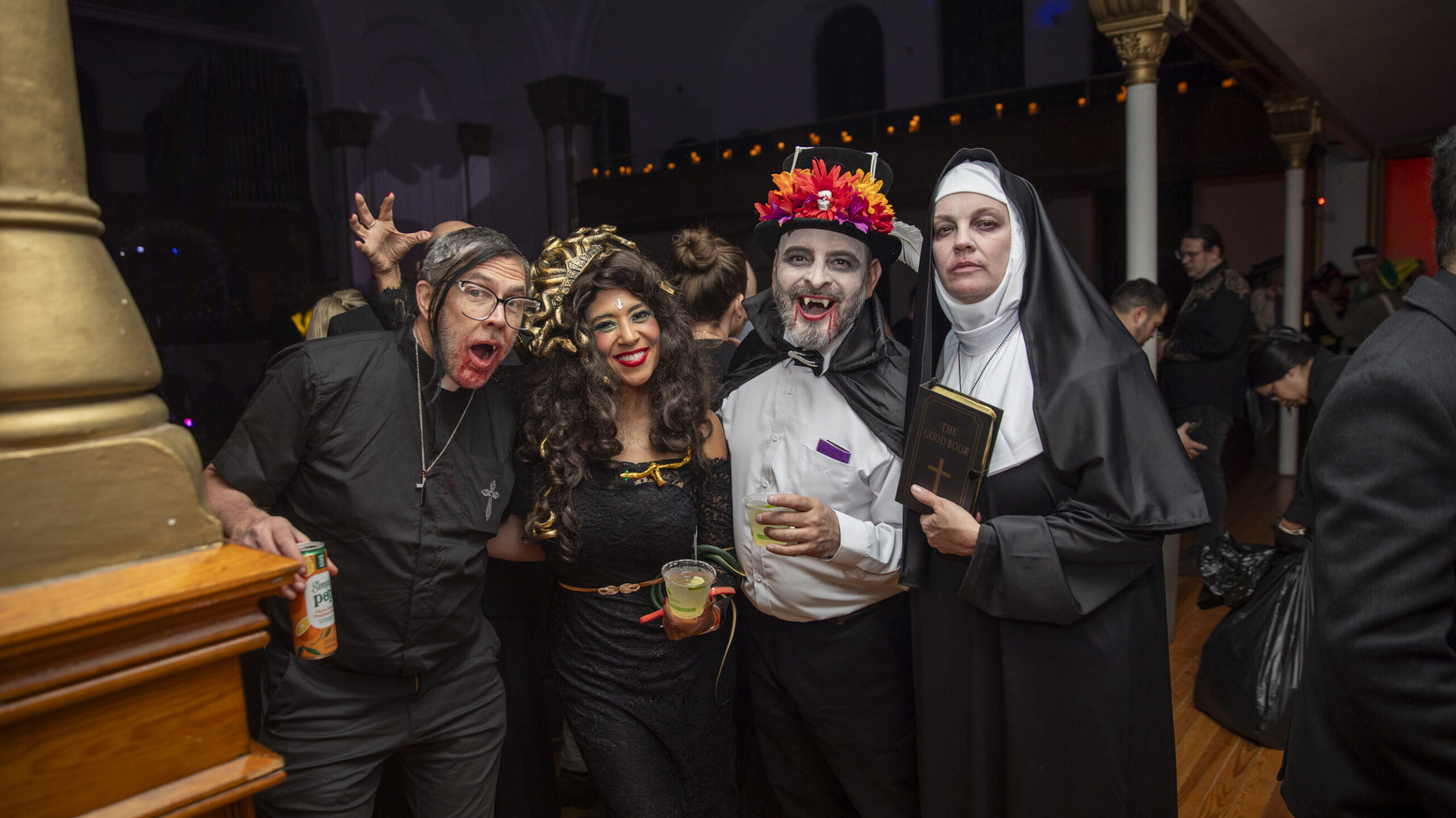 [gpt-4o]: Group in Halloween costumes at a party, including a vampire and nun holding a book labeled "The Good Book"