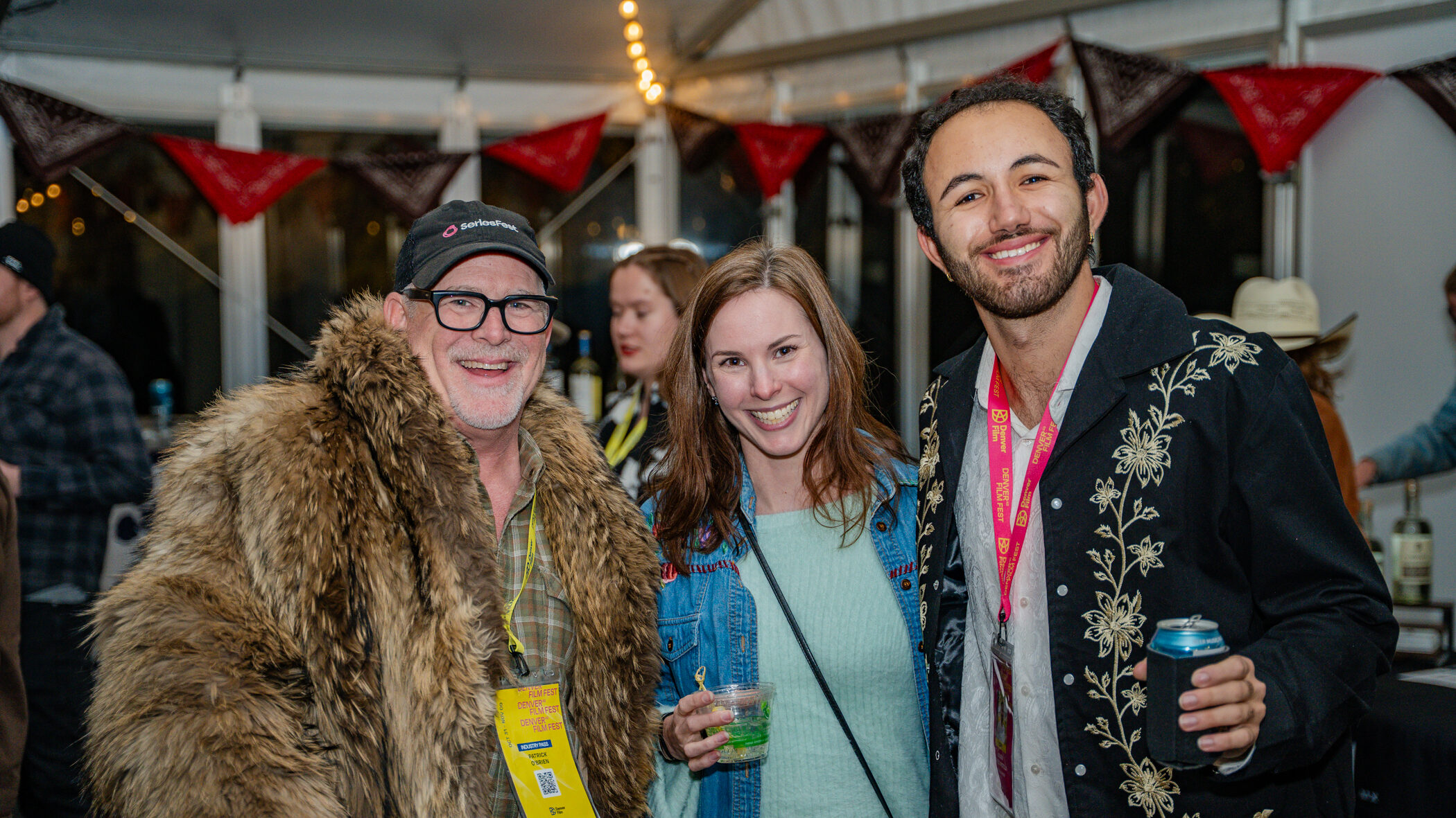 [gpt-4o]: DFF2025_Closing-Party_BNGU-56.jpg: Three people smiling, one in a fur coat, holding drinks at a party